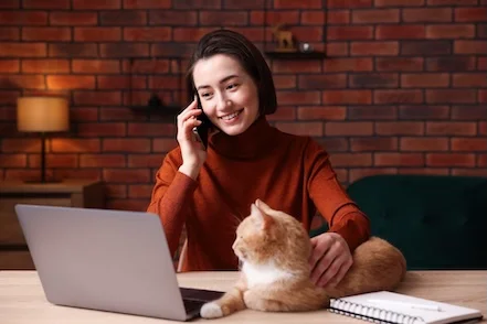 Donna che parla al telefono guardando il pc con accanto il suo gatto